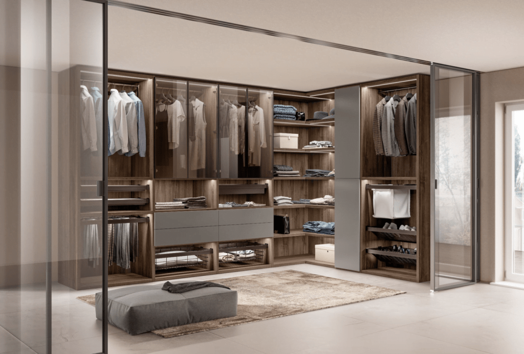 Spacious modern wardrobe with glass sliding doors and organized shelving units, showcasing clothes and accessories.