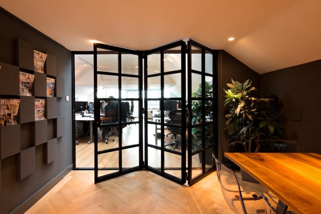 Stylish black steel-framed folding glass doors separating office space, with modern decor and indoor plants.