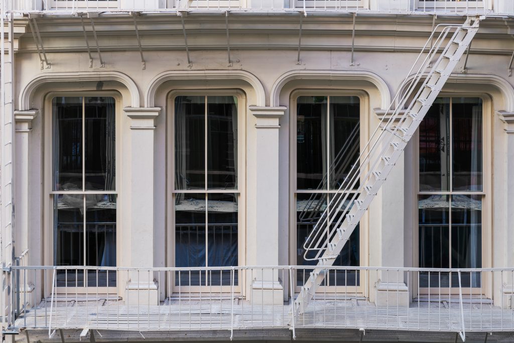 Classic facade of a historic building featuring large arched windows with vertical mullions, surrounded by ornate architectural detailing and a white metal fire escape structure.