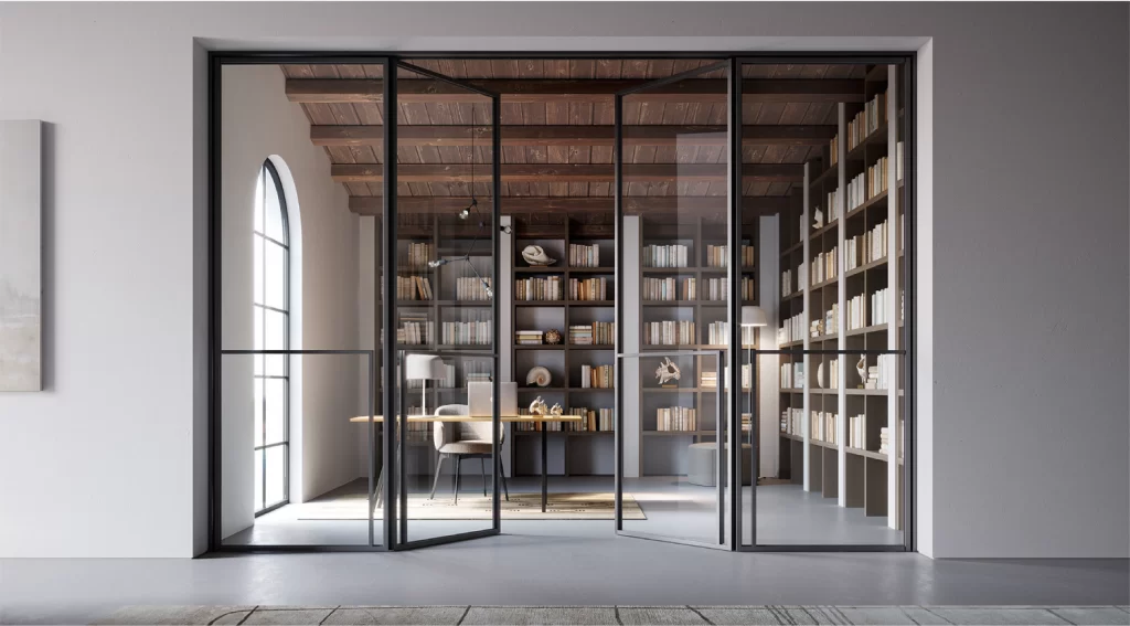 Home office with floor-to-ceiling steel-framed glass doors leading to a study room, featuring wooden bookshelves and a minimalist desk.