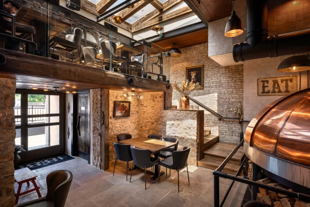 This restaurant interior highlights a charming and intimate space, blending industrial and rustic design with modern touches that beautifully marries the rustic charm of traditional materials with the sleekness of modern architectural features, resulting in a functional yet character-filled environment.