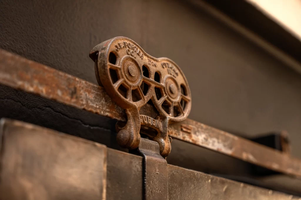 Rustic corten steel kitchen detail, showcasing an intricately designed vintage-style pulley system with weathered textures and embossed text, emphasizing the industrial aesthetic and the blend of raw, aged metal with functional design elements.