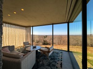 A modern sitting area with floor-to-ceiling glass walls offering a sweeping view of rolling hills and a wooded landscape